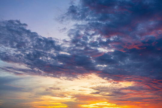 A breathtaking, vibrant sunset sky filled with dramatic, textured clouds painted in brilliant shades of fiery orange, deep magenta, and soothing twilight purple, capturing the serene beauty.