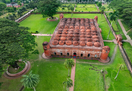 Aerial view of the Sixty Dome Mosque featuring numerous terracotta domes and lush green gardens with people walking on the paths in Bagerhat, Khulna Division, Bangladesh.
