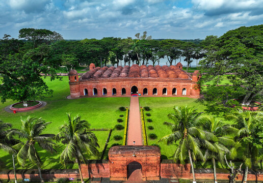 Aerial view of the Sixty Dome Mosque with its multiple terracotta domes, lush green gardens, and palm trees in Bagerhat, Khulna Division, Bangladesh.