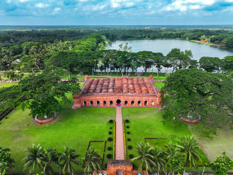 Aerial view of the Sixty Dome Mosque with its terracotta domes and lush gardens by a lake in Bagerhat, Khulna Division, Bangladesh.