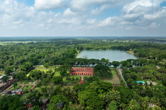 Aerial view of the historic Sixty Dome Mosque surrounded by lush green trees and a large pond under a cloudy sky in Bagerhat, Khulna Division, Bangladesh.