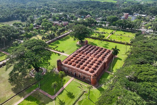 Aerial view of the Sixty Dome Mosque with its numerous terracotta domes, surrounded by lush green gardens and tropical trees in Bagerhat, Khulna Division, Bangladesh.