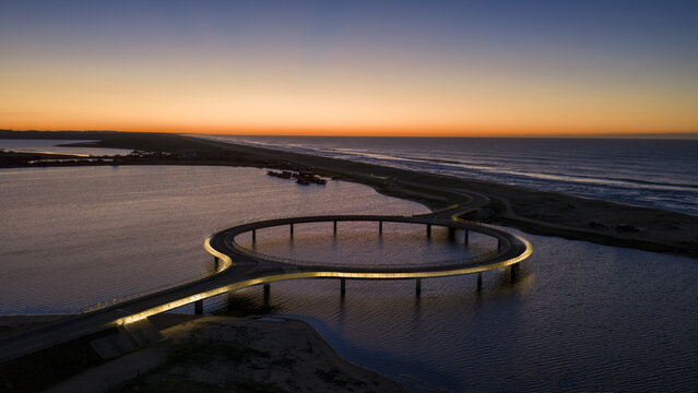 Aerial view of the illuminated circular Laguna Garzon Bridge over the calm water during a vibrant sunset Maldonado, Maldonado Department, Uruguay.