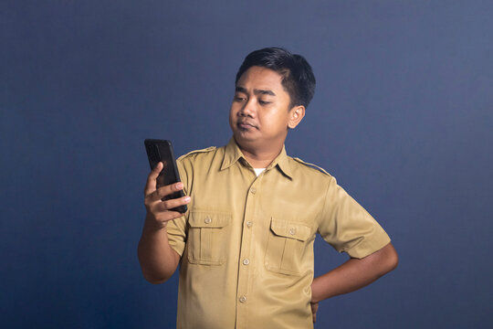 Indonesian civil servant man holding smartphone vertically looking at screen with indifferent face