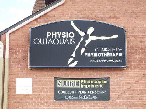 Gatineau, Quebec, Canada &ndash; May 1, 2026: A storefront sign for "Physio Outaouais" and a banner for "SURE Photocopies Imprimerie" are mounted on a brick wall at 729 boulevard St-Joseph.