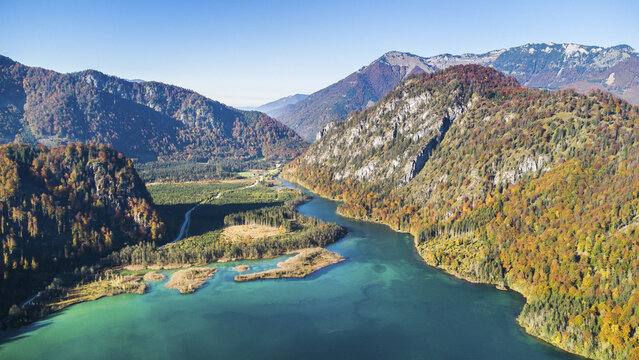 Aerial view of Almsee lake with turquoise water surrounded by steep mountains and colorful autumn forests under a clear blue sky Gmunden District, Upper Austria, Austria.