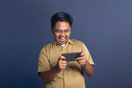 Indonesian civil servant man holding smartphone horizontally laughing happily playing mobile game
