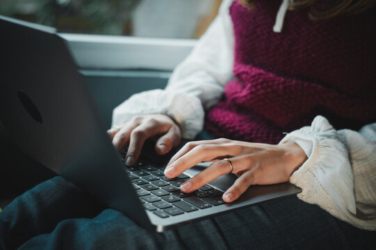 Hands of an anonymous woman using a laptop with a window in the background. Remote work and modern technology lifestyle concept.