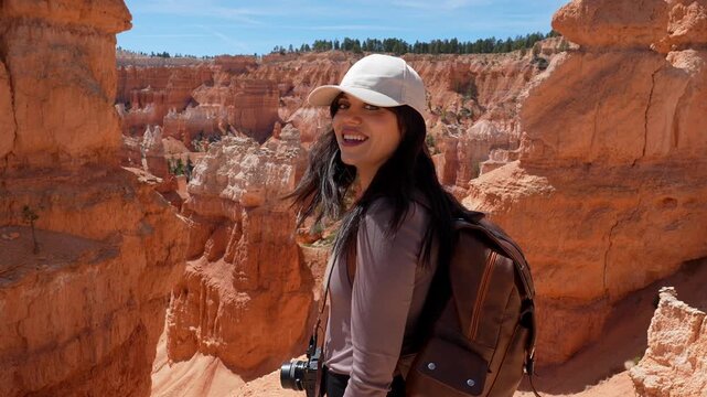 Young female traveler with a backpack hiking through the stunning red rock formations of bryce canyon national park, stopping to turn and smile at the camera on a sunny day in utah