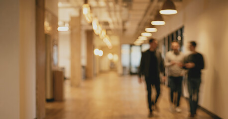 Fototapeta premium A blurred scene of three people walking in a modern office hallway with warm lighting, showcasing a collaborative and dynamic work environment.