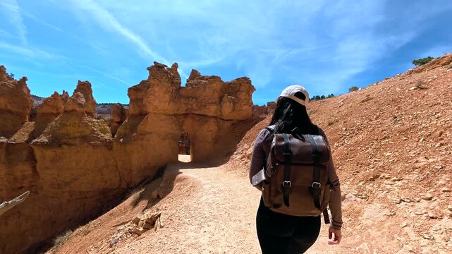 Adventurous young female photographer hiking the navajo loop and queen's garden trail, walking through unique rock formations in bryce canyon national park, utah, on a sunny day