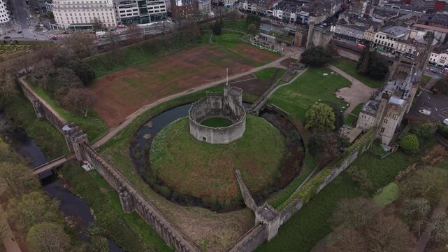 4K aerial video showing Cardiff Castle with its historic stone walls surrounded by green grounds in bright daylight.