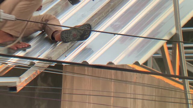 Construction worker installing metal roof sheets on a building frame using a power drill