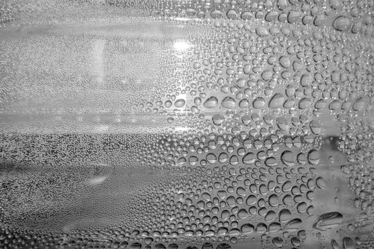 Monochrome abstract macro of condensation. Detailed water droplets on a transparent surface create a rhythmic, minimalist texture with high contrast. Focus on organic flow and repetition.