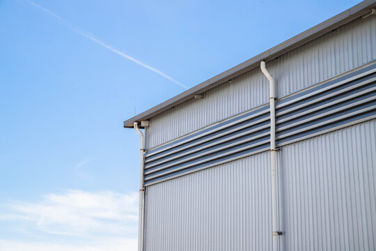Modern metal sheet factory wall and roof with blue sky background.Minimalist industrial building exterior with corrugated metal wall and rain gutters