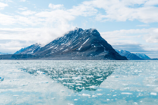 View of Lilliehookbreen with ice floes floating in the calm water and a snow-dusted mountain peak reflecting on the surface in Svalbard, Svalbard and Jan Mayen.