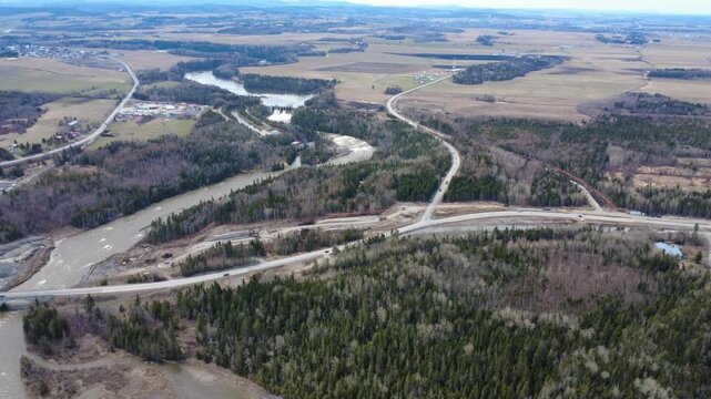 High-altitude drone footage of the Mitis River, Mitis-2 hydro station, farmland, and Route 132 construction during spring in Quebec, Canada.