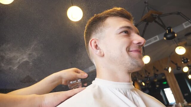 Hairdresser uses brush to cleaning client of cutted hair in barbershop. Male barber using a talc on neck of young guy in salon. Hairstylist doing cosmetic procedures for happy customer. Slow motion
