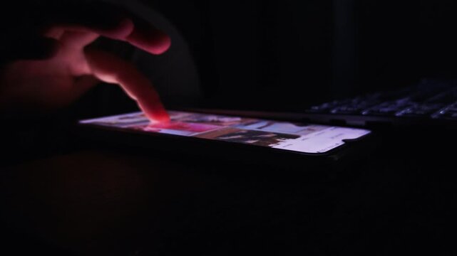 Finger scrolling through a mobile phone screen displaying social media content in a dark environment, highlighting digital connection, online activity, and modern communication data usage