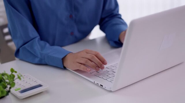 Asian business women hand typing laptop computer keyboard white desk calculator document financial report remote work home office professional bookkeeping