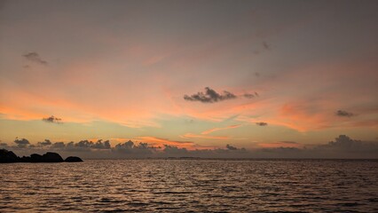 Fototapeta premium Colorful tropical ocean sunset with calm sea waves and soft clouds glowing in orange and pink evening light.
