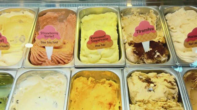 Gelato display showcasing a variety of colorful artisanal frozen desserts including strawberry sorbet, kumquat sugarcane, tiramisu, and more, attracting customers with diverse flavors