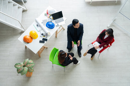 A diverse startup team stacks hands in unity during a planning session. The top view captures collaboration, innovation, and teamwork in a creative workspace with helmets, blueprints, and office tools