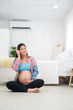 Pregnant woman sitting on floor in cozy modern home, listening to music with headphones, gently touching belly, maternity bonding, emotional wellness, prenatal care, lifestyle, motherhood, relaxation