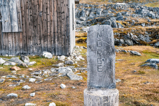 View of a wooden marker with NORGE carved into it near a weathered cabin in the rocky tundra of Varsolbukta, Svalbard, Svalbard and Jan Mayen.