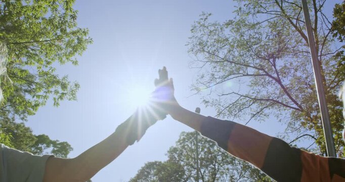 Children give high five after rollerblade practice in park. Brother and sister raise hands together celebrating progress after learning to skate during sunny day