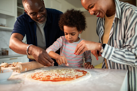 Parents and child making homemade pizza in kitchen
