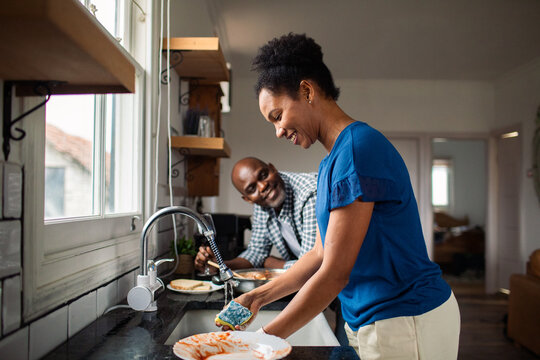 Smiling couple washing dishes together in home kitchen