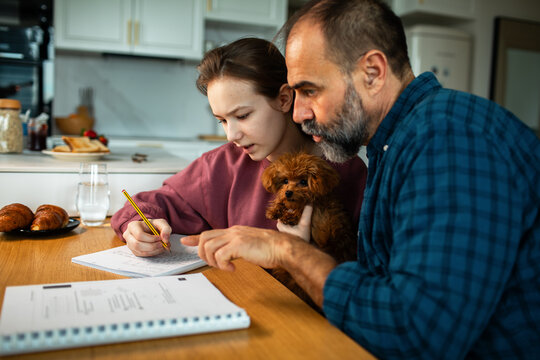 Father helping teenage daughter with homework at kitchen table