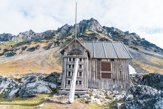 View of the historic trapper cabin at Varsolbukta nestled against a rugged mountain backdrop with rocky terrain and sparse arctic tundra in Svalbard, Svalbard and Jan Mayen.