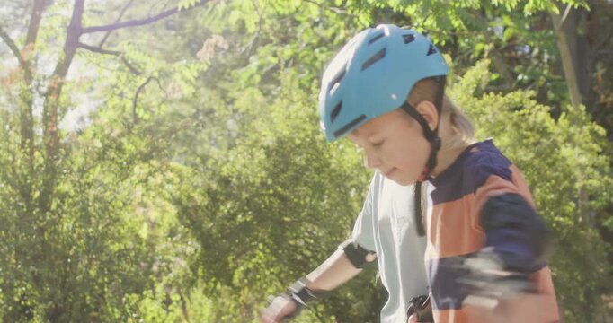 Boy holds sister hand while learning to skate on park path. Preschooler child keeps knees bent trying to balance on rollerblades with careful sibling support nearby