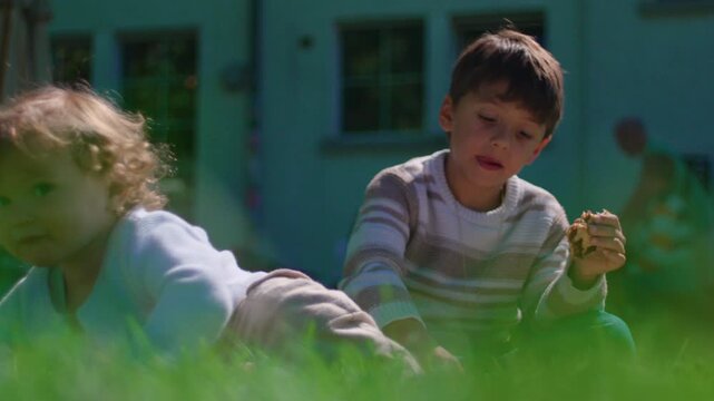 Older brother pushing toddler sibling aside while sitting on sunny grass lawn during outdoor picnic conveying childhood conflict sibling rivalry emotional tension and family dynamics