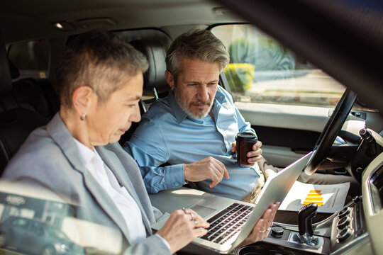 Senior business colleagues reviewing data on laptop in car