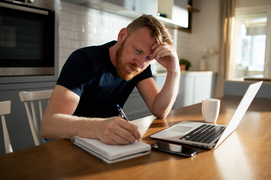 Thoughtful man writing notes while working from home at kitchen table