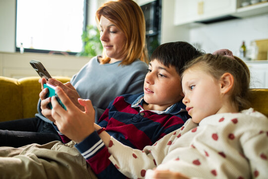 Mother and children using smartphones on couch at home