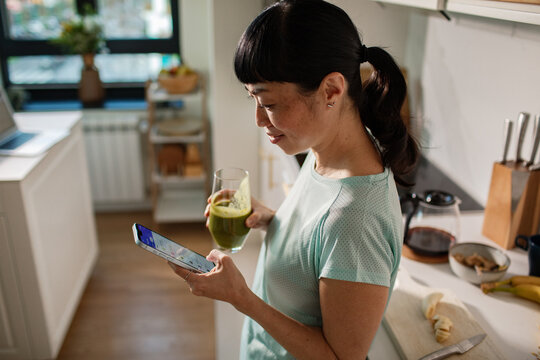 Woman checks phone while drinking green smoothie in a home kitchen