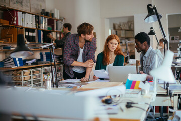 Young creative team collaborating at laptop in open plan design studio © Geber86