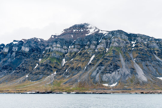 View of the rugged mountains of Varsolbukta with snow patches and rocky slopes along the coast in Svalbard, Svalbard and Jan Mayen.