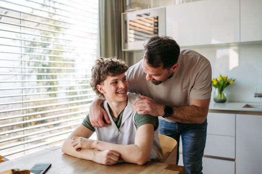 Father supporting teenage son at home during everyday moment.
