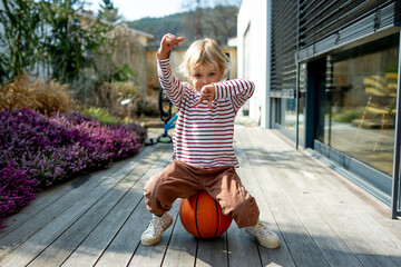 Toddler boy playing with basketball outdoors in backyard near home.