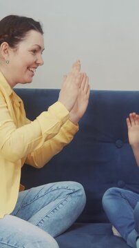 A woman and a boy are playing a hand-clapping game on a blue couch. They smile as they enjoy their playful interaction, emphasizing connection and joy.