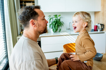 Obraz premium Dad feeding toddler during family mealtime in modern kitchen.