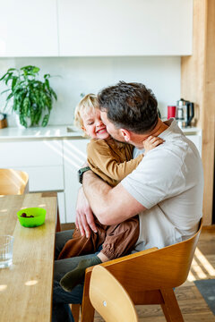 Dad feeding toddler during family mealtime in modern kitchen.