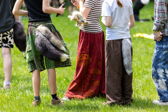 Group of young therians wearing furry tails and animal accessories gathers in sunny park. Playful quadrober community scene with cosplay fashion, fantasy roleplay and creative outdoor lifestyle