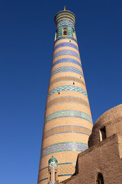 Islam Khoja Minaret in Khiva with colorful tilework bands against a clear blue sky. Ideal for travel guides, cultural publications, and tourism marketing about Uzbekistan.