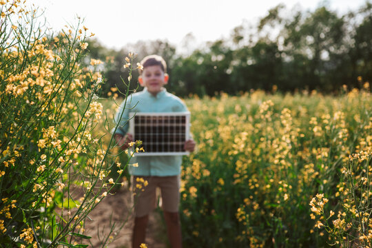 Boy holding solar panel in blooming field with sustainability concept.